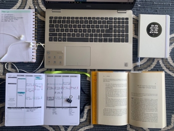 Computer, planner, notes, and book sitting on a table